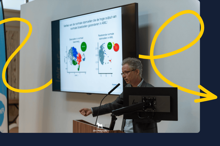 Volwassen man achter een microfoon met informatie op een televisie scherm.